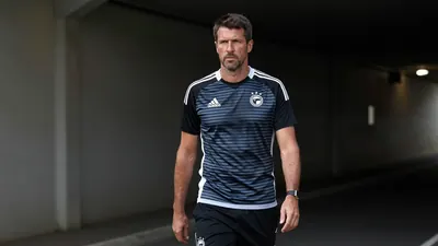 Low-key floodlight-lit image of a ruggedly-built, 35-year-old male coach, standing in the tunnel of MCH Arena, wearing a...
